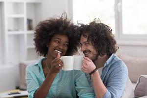 pareja multiétnica sentada en un sofá en casa bebiendo café foto