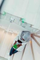 Young african modern muslim woman using tablet computer while sitting on the stairs at home wearing hijab clothes top view photo