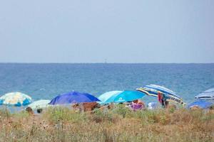 gente tomando el sol bajo las sombrillas en la playa foto