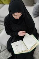 Portrait of young muslim woman reading Quran in modern home photo