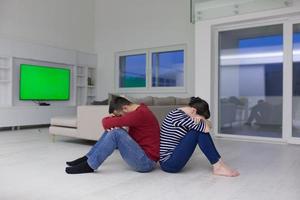 young couple sitting with back to each other on floor photo