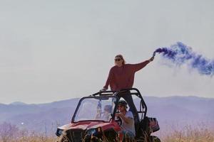 gente emocionada divirtiéndose disfrutando de un hermoso día soleado sosteniendo antorchas coloridas mientras conduce un coche de buggy fuera de la carretera foto