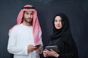 muslim couple using modern technology in front of black chalkboard photo