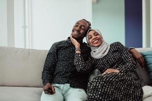 African Couple Sitting On Sofa Watching TV Together. Woman Wearing Islamic Hijab Clothes photo
