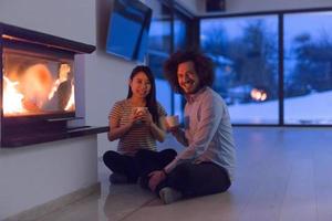 happy multiethnic couple sitting in front of fireplace photo