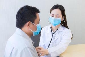 Both of Asian woman doctor and a man patient wear medical face mask to protect infectious disease Covid 19 while check up health in hospital. photo