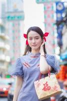 hermosa chica asiática vestida de chino está sonriendo sostiene la bolsa de tela que proyecta la palabra que significa feliz y caminando en la calle en la ciudad de china, tailandia. foto