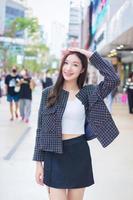 Portrait of a beautiful, long-haired Asian female in a black pattern coat with braces on teeth while she put her hand on head walking and smiling outdoors in the city. photo