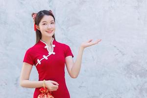 Asian beautiful confident woman in red dress stands holding a red bag is pointing hand to present something on the dark gray wall in Chinese new year theme. photo