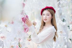 hermosa mujer asiática con el pelo largo de bronce en camisa blanca de manga larga sonríe y se para en el jardín de flores de rosas blancas como un tema natural y lujoso