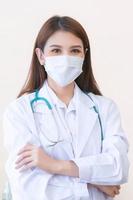 Asian female doctor stood wearing a white robe, wearing a mask and stethoscope. photo