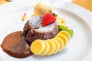 un plato de postre llamado lava de chocolate, incluye helado de vainilla, plátano, kiwi y manzana. este dulce está hecho a base de semilla de cacao. buena combinación entre bizcocho de chocolate, helado frío y frutas. foto