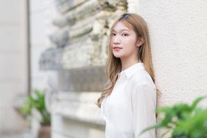 Portrait Asian beautiful woman with long bronze hair in white long sleeve shirt stand smile in an urban outdoor park. photo