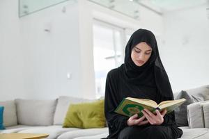 Portrait of young muslim woman reading Quran in modern home photo