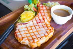 A pork chop is a loin cut taken perpendicular to the spine of the pig. It is served with black pepper gravy sauce, mashed potatoes and salad on wood plate. photo