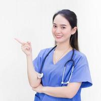 Asian beautiful woman doctor in a blue uniform stands and smiles while pointing to the top on a white background. photo