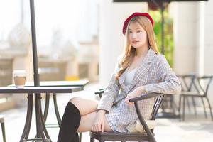 Asian beautiful  woman who wears suit and red cap with bronze hair sits on chair in coffee shop while there was a coffee mug on the table on a sunny morning. photo