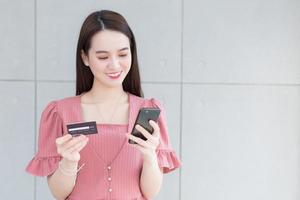 Asian business woman who wears pink dress holds smartphone and credit card in her hands in finance choice theme. photo