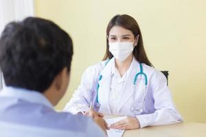 Asian woman doctor asking patient questions in the clinical examination room at the hospital by wearing a surgical mask at all times in health care and coronavirus protection concept. photo