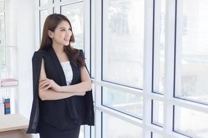 A Asian female smiling and  looking out of the window with arm crossed. photo