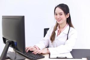 Asian woman doctor is typing on keyboard to record information into computer while she wears medical face mask in hospital. photo