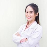 Asian woman doctor who she has a black long hair, wear a stethoscope and a white lab coat as a uniform while arm cross at office room in hospital in health care,new normal and protection concept. photo