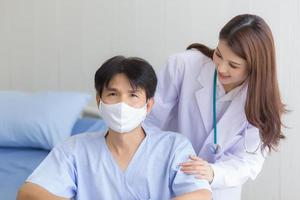 Asian doctor woman talking with a man patient who wear face mask about his health symptom while he sit on wheelchair at hospital. photo