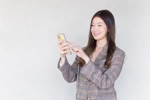 Asian professional woman with black long hair wearing a plaid suit and pretty happily using a smartphone on a white background. photo