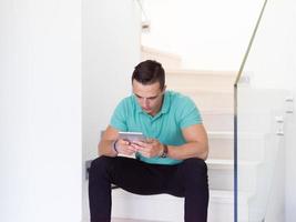man using a tablet while sitting on the stairs at home photo