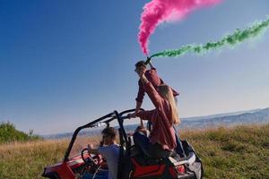 excited people having fun enjoying beautiful sunny day holding colorful torches while driving a off road buggy car photo