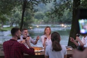 friends toasting red wine glass while having picnic french dinner party outdoorcameraman records a group of friends having lunch photo