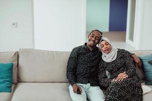 African Couple Sitting On Sofa Watching TV Together. Woman Wearing Islamic Hijab Clothes photo