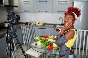 African american woman filming her blog broadcast about healthy food at home kitchen and making picture on phone. photo