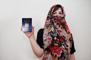 joven musulmana árabe vestida con hiyab tiene pasaporte de la república de irak sobre fondo de pared blanca, retrato de estudio. foto