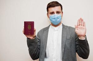 European man in formal wear and face mask, show Denmark passport with stop sign hand. Coronavirus lockdown in Europe country concept. photo