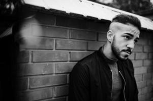 Portrait of stylish arab beard man wear grey turtleneck and black jaket. Arabian model guy against brick wall. photo