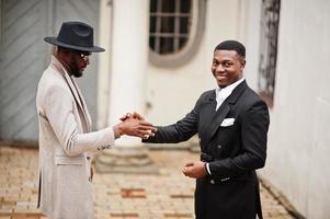dos hombres negros de moda se dan la mano. retrato de moda de modelos masculinos afroamericanos. llevar traje, abrigo y sombrero. foto