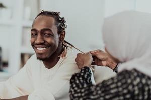 A young Muslim couple has a romantic time at home while the woman makes the hairstyle for her husband female wearing traditional Sudan Islamic hijab clothes. photo