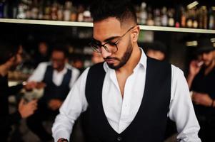 Stylish arab man against group of handsome retro well-dressed guys gangsters spend time at club, drinking on bar counter. Multiethnic male bachelor mafia party in restaurant. photo