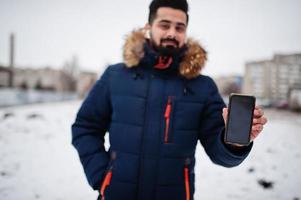 Beard indian man wear jacket in cold winter day. He speak mobile phone by wireless headphones. photo