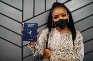 African american woman wearing black face mask show Nicaragua passport in hand. Coronavirus in America country, border closure and quarantine, virus outbreak concept. photo