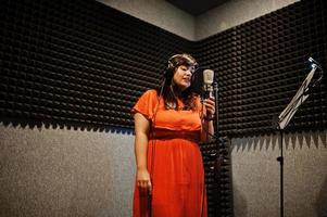 Young asian singer with microphone recording song in record music studio. photo
