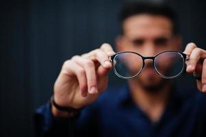 Middle eastern entrepreneur wear blue shirt show close up eyeglasses, against steel wall. photo