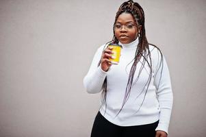 glamorosa mujer afroamericana en suéter de cuello alto blanco posan en la calle con una taza de café a mano. foto