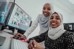 Friends at the office two young Afro American modern Muslim businesswomen wearing scarf in creative bright office workplace with a big screen photo