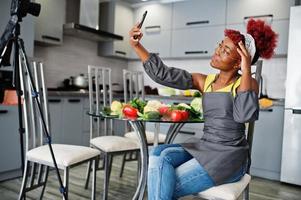African american woman filming her blog broadcast about healthy food at home kitchen and making selfie at phone. photo