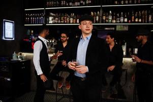 Stylish arab man against group of handsome retro well-dressed guys gangsters spend time at club, drinking on bar counter. Multiethnic male bachelor mafia party in restaurant. photo