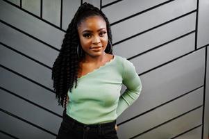 Portrait of attractive young african american woman wearing in green sweater posing against grey wall. photo