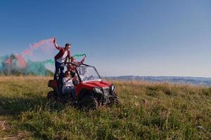 excited people having fun enjoying beautiful sunny day holding colorful torches while driving a off road buggy car photo