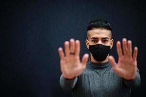 Middle eastern man in gray turtleneck and black face protect mask on isolated background show two hands, stop sign. photo